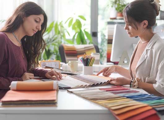 Interior designer and customer sitting at office desk, they are checking fabric swatches and picking colors